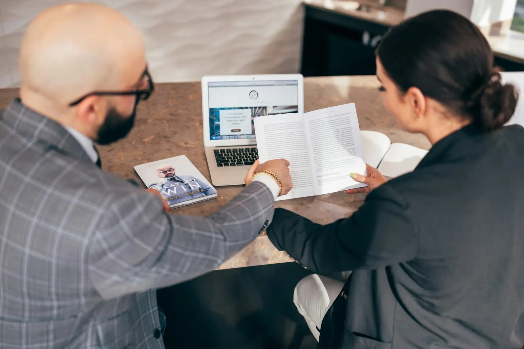 An adviser going through a printed report with a client across a desk, a laptop open between them.