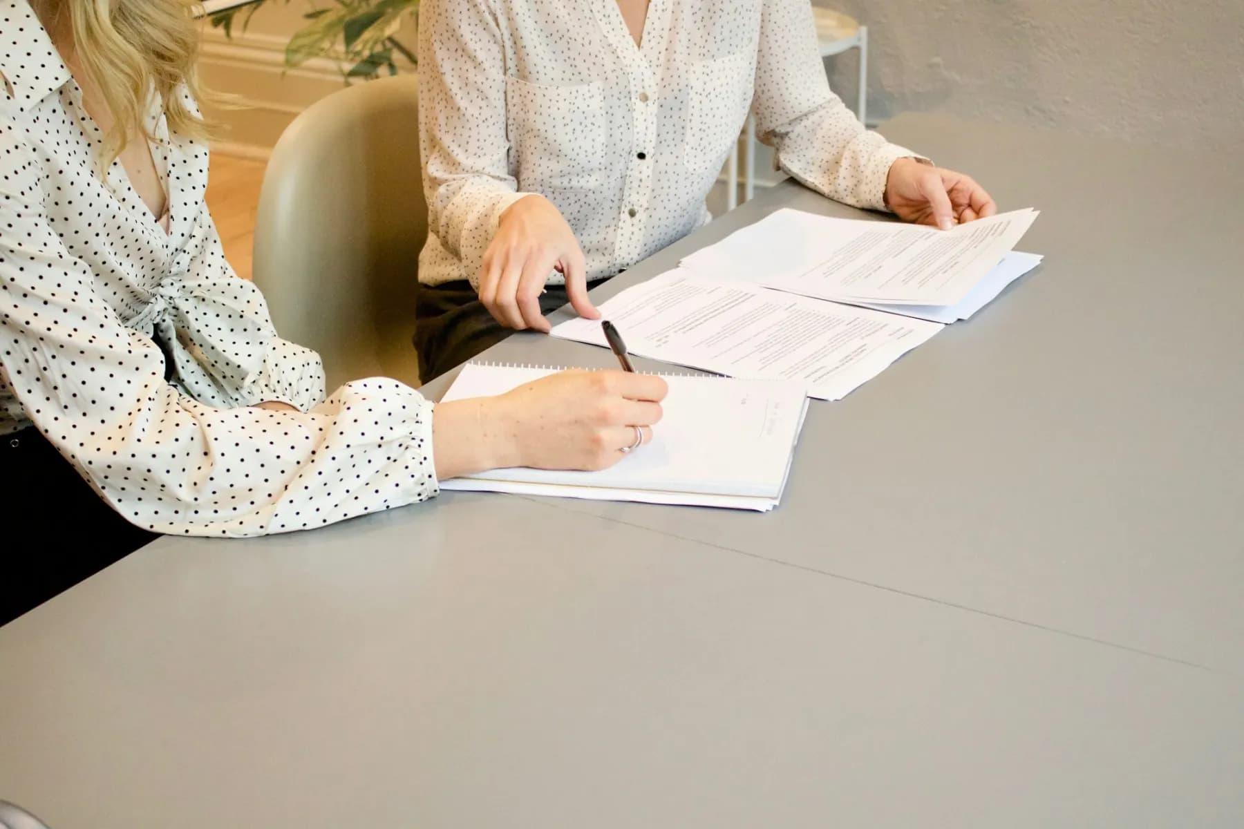 Two people at a table, one signing a printed document.